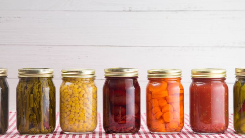 A row of canning jars with tighly-sealed canning lids with various homegrown foods inside.