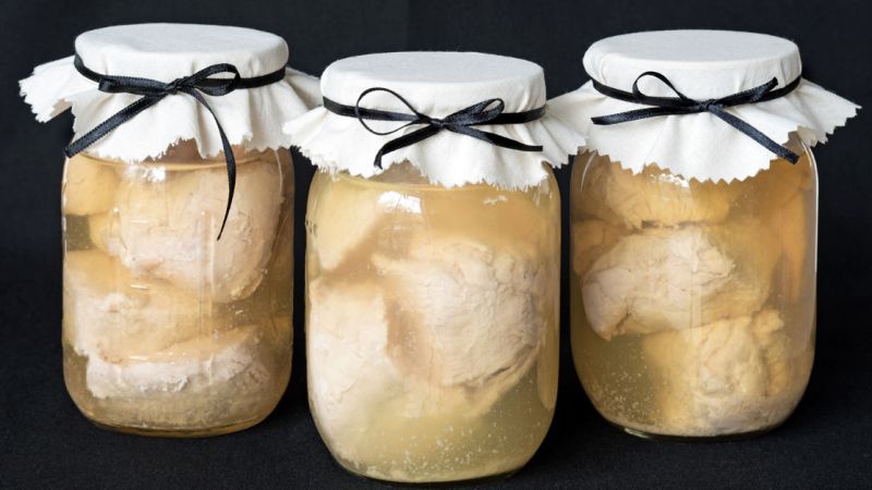 Cans of raw chicken prepared for storage sit on a black table.