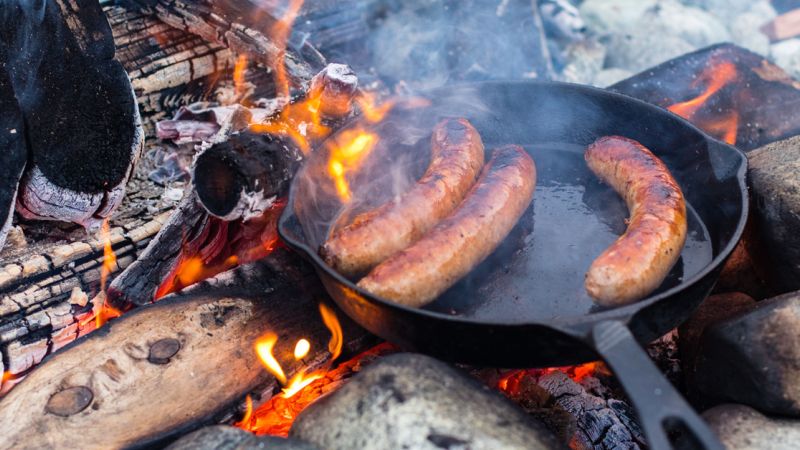 Cleaning a cast iron skillet after cooking sausages over an open fire .