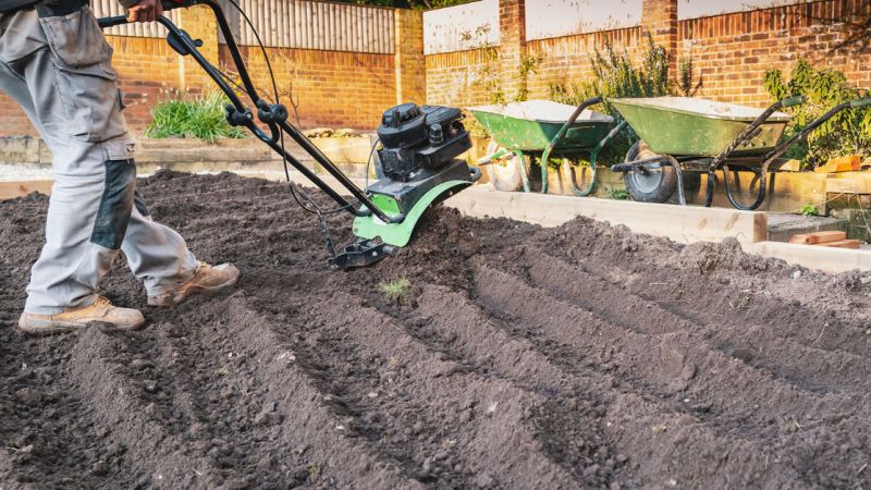 A man uses a garden till to prepare his homestead garden for the planting season.