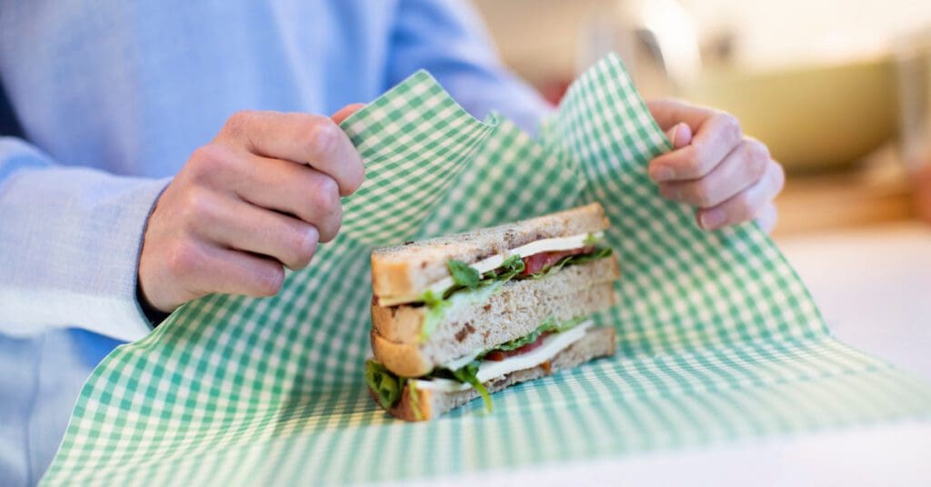 A man uses a beeswax wrap to pack his sandwich for lunch. 