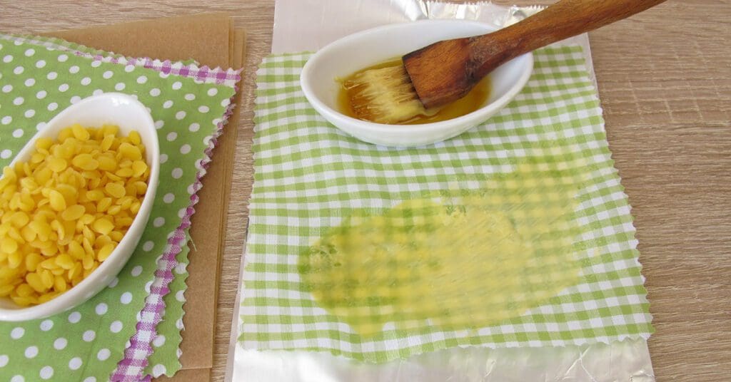 A person spreads homemade beeswax wrap coating on a piece of 100% cotton fabric. 