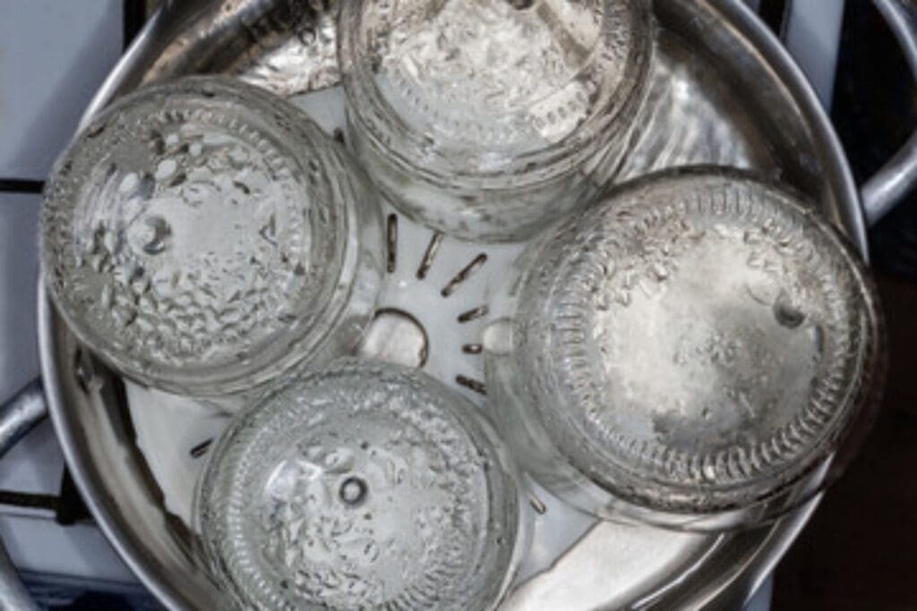 Canning jars are in a pot of boiling water on the stove to sterilize them before using them to can raw chicken. 
